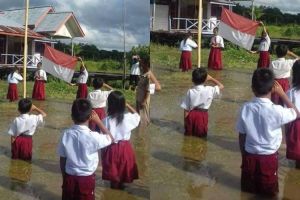 Siswa-siswa SD ini khidmat upacara bendera di tengah banjir