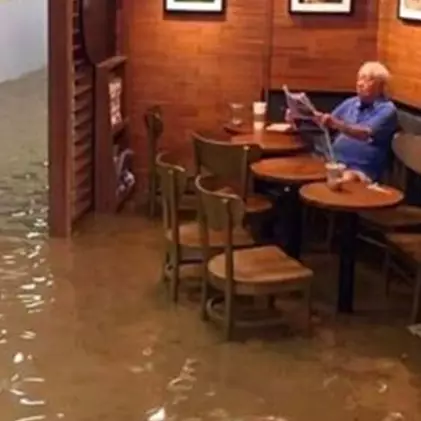 Tak peduli ada banjir besar, kakek ini tetap santai menyeruput kopi